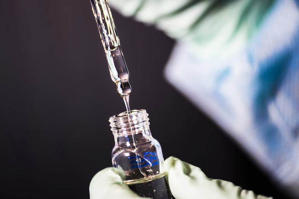 Gloved hand releasing a drop from a glass pipette into a sample vial
